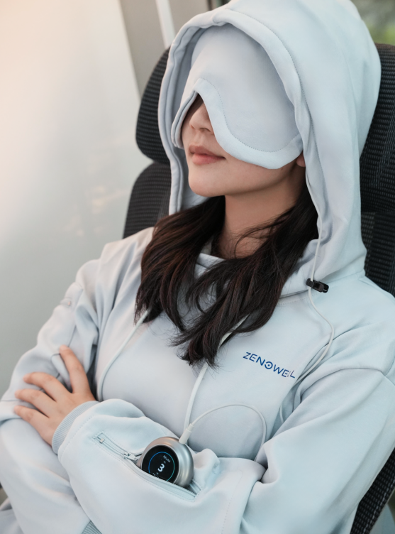 Person wearing a ZenoWell hoodie and eye mask while using a ZenoWell wearable device luna during a rest session.